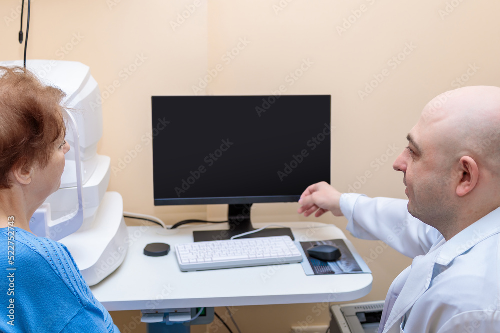 A male ophthalmologist explains the results of an eye examination to an adult woman, showing a drawing on a computer. A male ophthalmologist explains the results of an eye examination to an adult woman, showing a drawing on a computer.