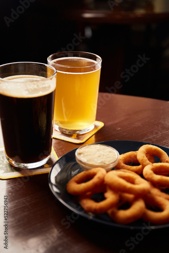 Crispy, golden onion rings sprinkled with sea salt in a bowl And beer glasses on a wooden table.