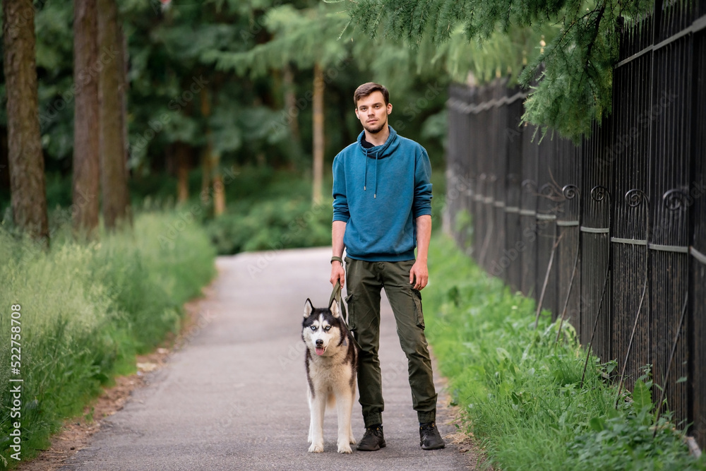 A cute young man is walking along the road with his beloved Siberian Husky dog in nature.
