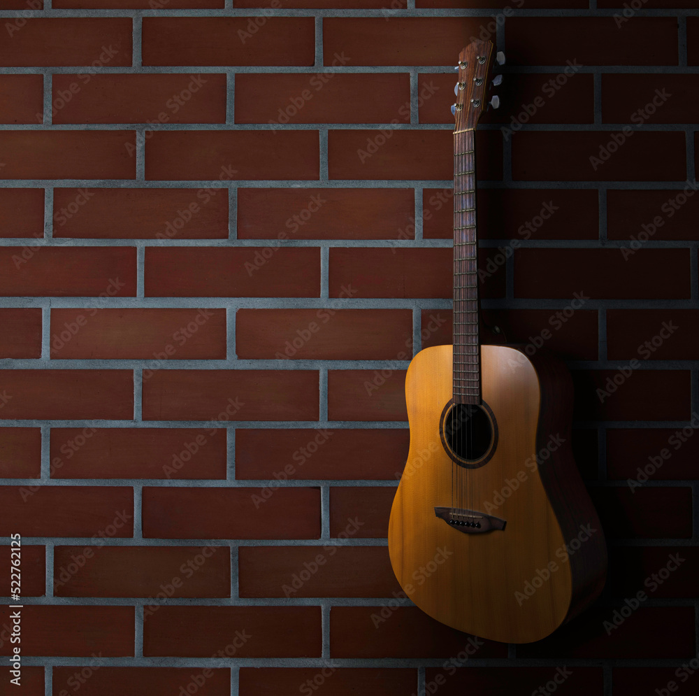 brown acoustic guitar stand in front of brick wall background. Guitar body part front made with top solid, side and back mahogany wood. brown acoustic guitar stand in front of brick wall background. Guitar body part front made with top solid, side and back mahogany wood.