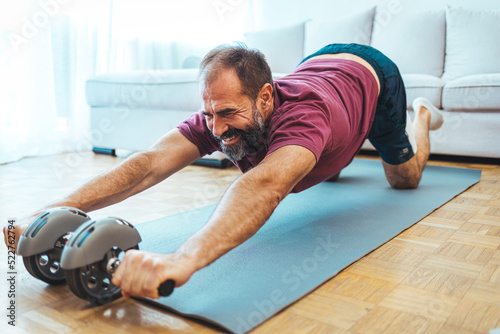 Senior man working out at home, watching youtube videos and learning the exercises. Mature man exercising at home - watching virtual exercise class on laptop.