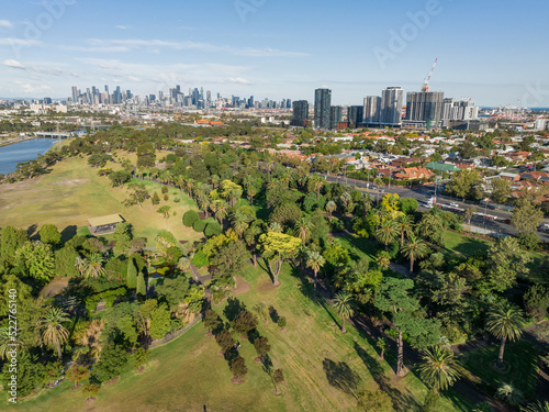Aerial view of treed parkland alongside a river with city buildings behind
