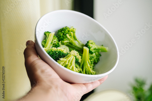 Hand holding a bowl of cooked green broccoli. Boiled broccoli vegetable in white small bowl for healthy food concept