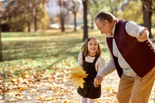 Little girl spending time with grandfather at the park in autumn
