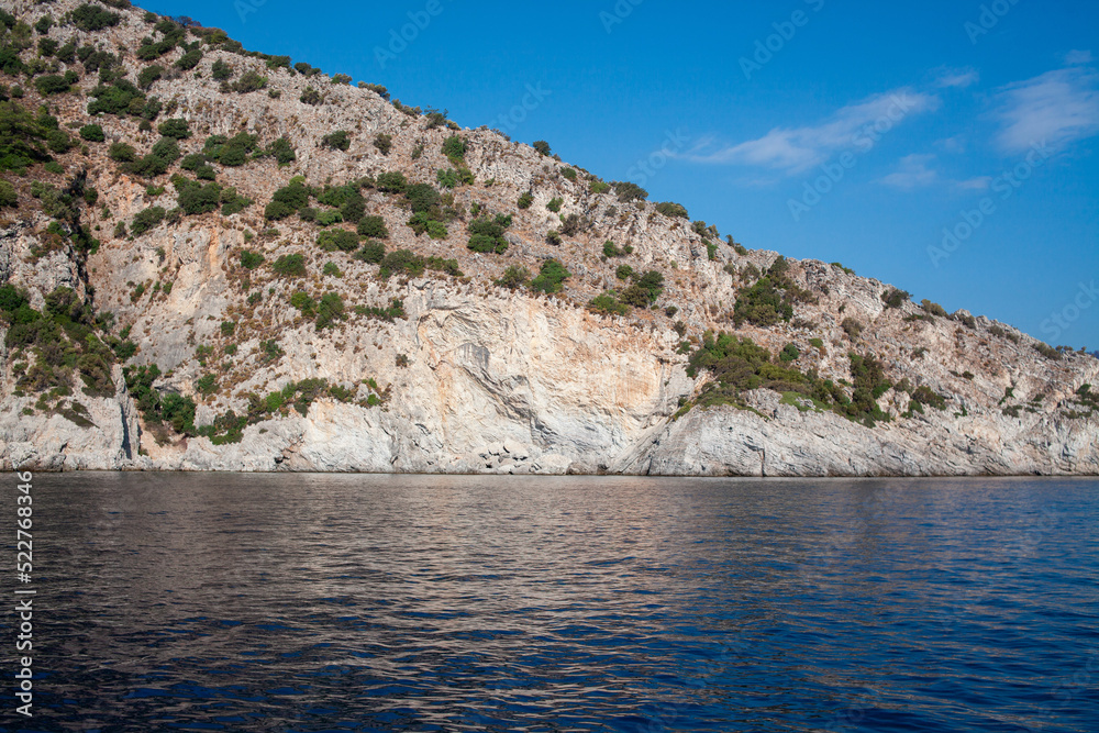 Mediterranean rocky shores with green trees and landscape. View from sea. Rock reflection in blue water sea