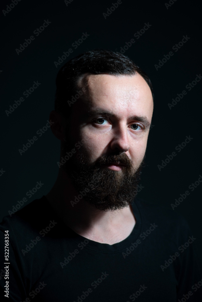 dramatic portrait of bearded millennial on black background