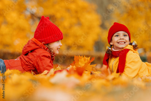 Two girls are lying on a red and yellow leaves in an autumn park. Warm bright autumn and good mood.