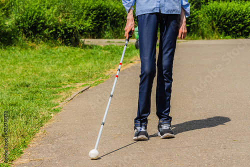 Underfed blind woman with swollen joints and wrists because of arthritis, taking a walk in a park with walking cane on asphalt