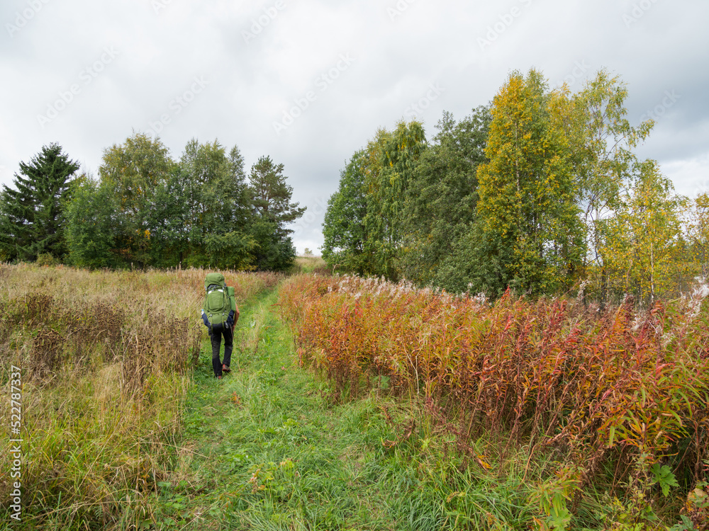 Backpacker goes on country road. Man with touristic rucksack is hiking in summer or autumn season. Active lifestyle. Outdoor leisure activity. Backpacker goes on country road. Man with touristic rucksack is hiking in summer or autumn season. Active lifestyle. Outdoor leisure activity.