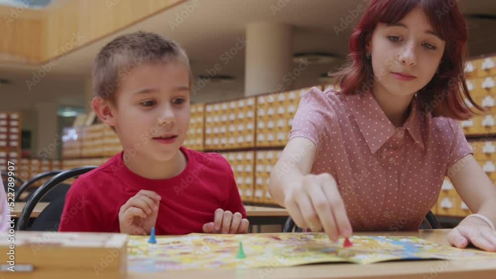 4K. Children play a board game in the library, sitting at the table. 4K. Children play a board game in the library, sitting at the table.
