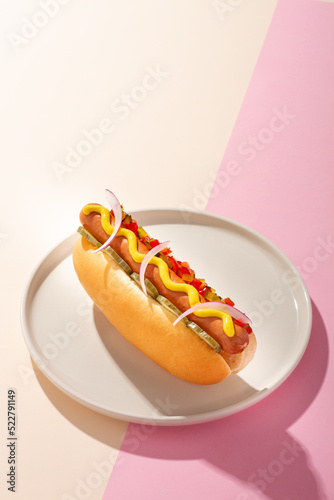 Hot dog in a round plate on white and pink background