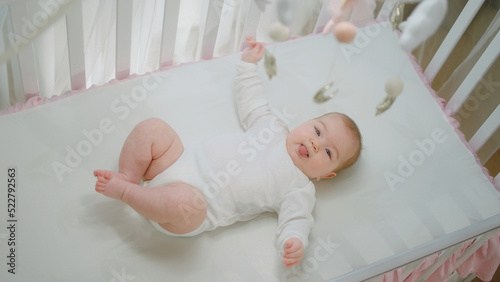 Wallpaper Mural Amazing cute baby girl alone in her baby cot playing with hands and legs and looking up the cot toys concept of baby and childhood Torontodigital.ca