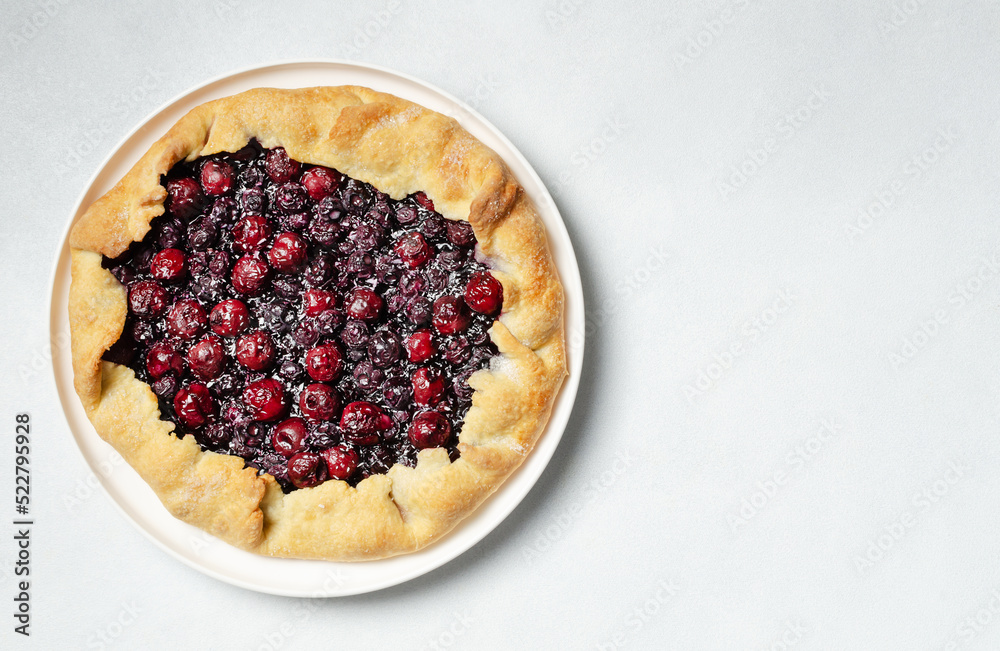 Fresh cherry and blueberry galette with coconut on white plate, top view, copy space, white background. Homemade rustic dessert - american pie or tart or cake or french galette Fresh cherry and blueberry galette with coconut on white plate, top view, copy space, white background. Homemade rustic dessert - american pie or tart or cake or french galette