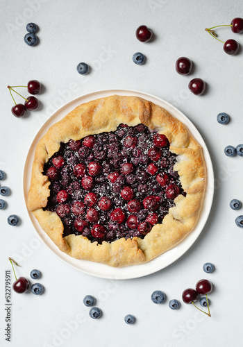 Fresh cherry and blueberry galette with coconut on white plate, top view, white background. Homemade rustic dessert - american pie or tart or cake or french galette