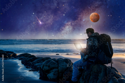 silhouette of digital nomad sitting with laptop on the beach outdoors working under the starry night and milky way