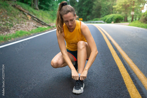 Runner woman tying laces for jogging run on forest road. Female athlete getting ready for training exercise. Motivation health and fitness exercise. Sport lifestyle concept. Copy space banner