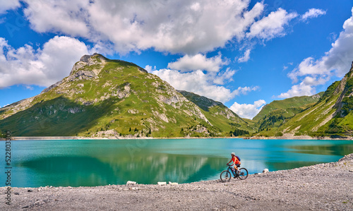 active senior woman, riding her electric mountain bike at Spuller Lake in the Arlberg area near the famous village of Lech, Tirol, Austrian Alps © Uwe