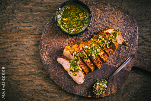 Homemade grilled pork steak with chimichurri verde sauce on cutting board on dark background photo