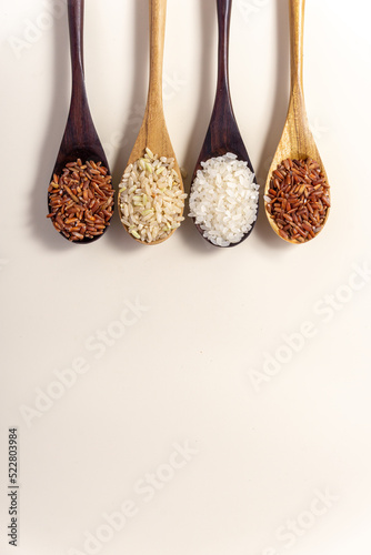 Raw and uncooked rice assortment in wooden spoon on white background. Place for text. Top view.