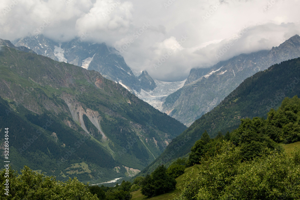 Panoramic view of the green and snowy mountains at the exit of the city of Mestia, during the trek to Ushguli, in Geogia.
