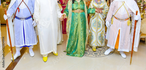 A groom in a djellaba holds the hand of his bride who is wearing a kaftan