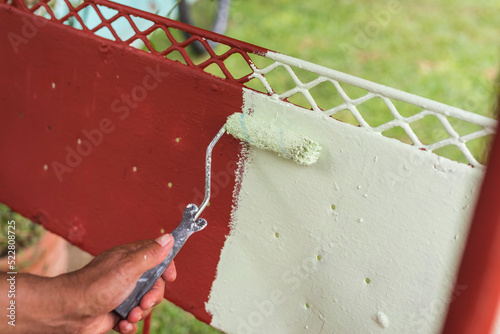 Applying a layer of light green colored quick dry enamel paint on top of another red oxide primer coat. Painting a restored glider swing with a small roller. photo