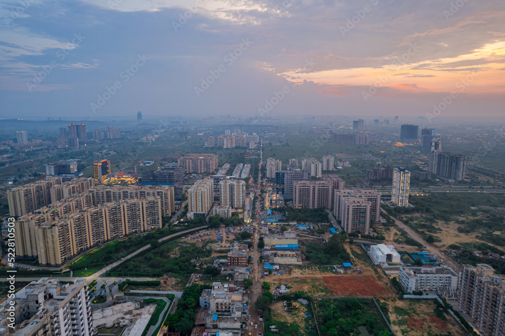 drone aerial shot showing busy traffic filled streets between skyscrapers filled with houses, homes and offices with a red sunset sky showing the hustle and bustle of life in Gurgaon, delhi