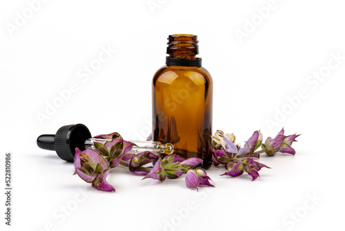 A bottle of essential oil with fresh blooming clary sage twigs on white background.