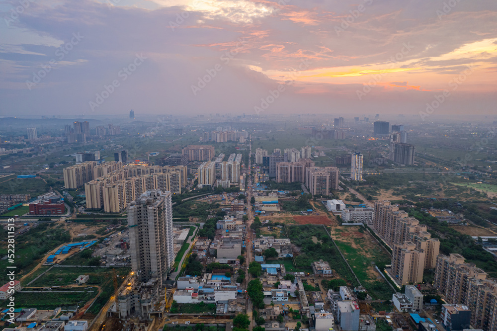 drone aerial shot showing busy traffic filled streets between skyscrapers filled with houses, homes and offices with a red sunset sky showing the hustle and bustle of life in Gurgaon, delhi