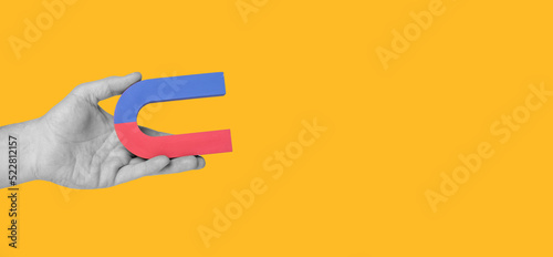 Banner with hand holding horseshoe magnet on orange background. Place for text. Affection force or physics concept. High quality photo