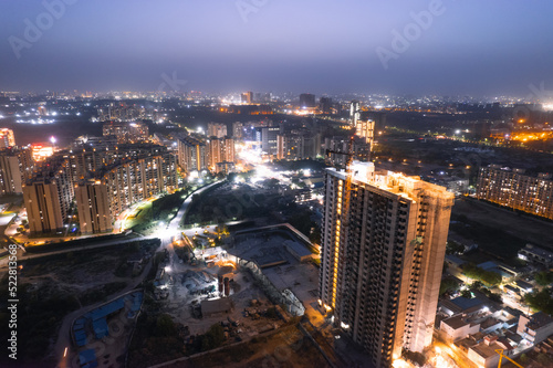 aerial drone dusk twilight shot showing orange lights of streets, homes and markets surrounding a skyscraper with the city scape stretching into the distance in gurgaon haryana delhi photo