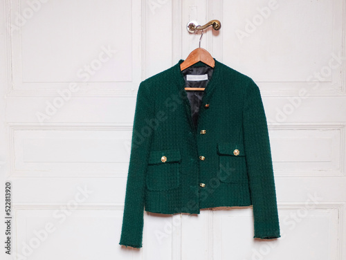 Stylish women's trendy green jacket with gold large buttons hangs on a wooden coat hanger photo