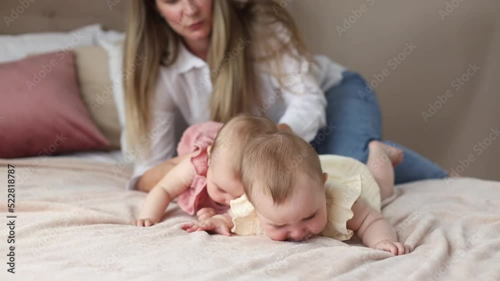 Lifestyle young mother soothes and cares for two crying and naughty little twins 6 months old on a bed in a cozy home Lifestyle young mother soothes and cares for two crying and naughty little twins 6 months old on a bed in a cozy home