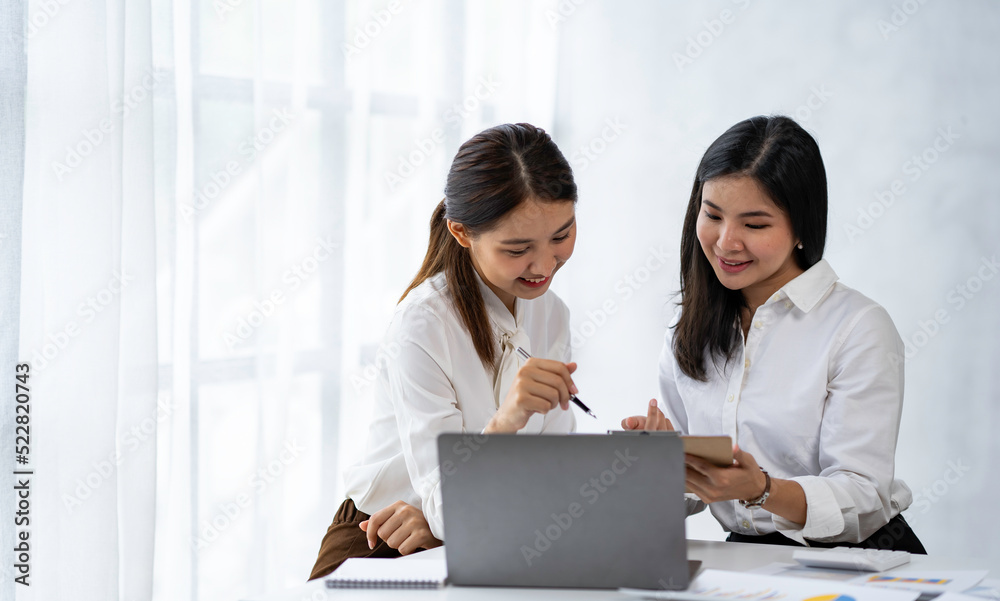Two young Asian businesswomen talk, consult, discuss working with new startup project idea presentation analyze plan marketing and investment in the office. Two young Asian businesswomen talk, consult, discuss working with new startup project idea presentation analyze plan marketing and investment in the office.
