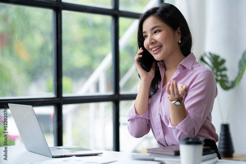 Beautiful Asian businesswoman smiling and talking on the phone holding customers talking and answering business questions at an office desk. Beautiful Asian businesswoman smiling and talking on the phone holding customers talking and answering business questions at an office desk.