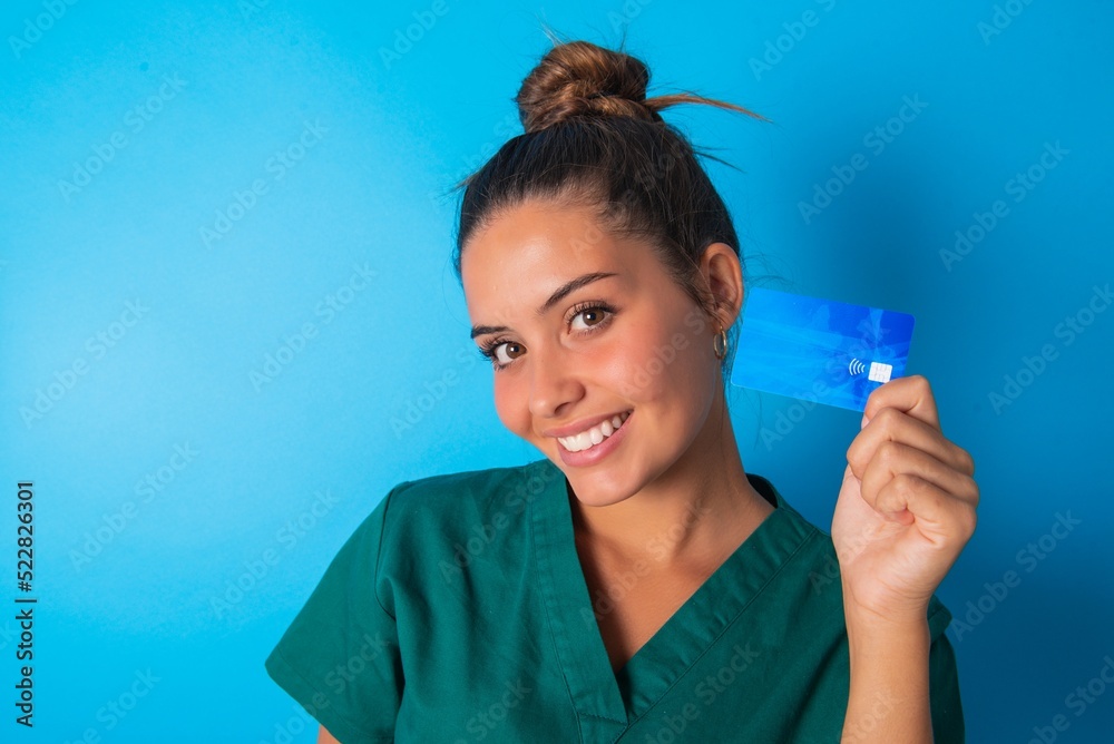Close up photo of optimistic beautiful doctor woman wearing medical uniform over blue background hold card Close up photo of optimistic beautiful doctor woman wearing medical uniform over blue background hold card