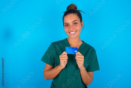 Photo of beautiful doctor woman wearing medical uniform over blue background positive smile hold credit card income salary
