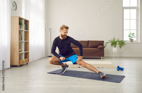 Happy sporty Caucasian guy in sportswear warmup before training session on lockdown at home. Smiling toned man do sports workout exercise indoors, follow healthy lifestyle. Physical activity.