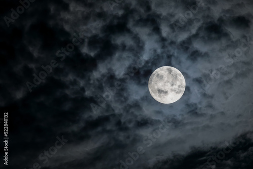 Full moon at night. The illuminated face of the moon is wrapped in a cloud cover that covers it in a veiled way.