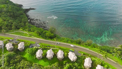 Cinematic ocean shore shot with cars with tourists driving to the summer beach rentals, vacation beach cottages for perfect holiday in paradise 4K drone. Aerial Hanalei Bay villas, Princeville Hawaii photo