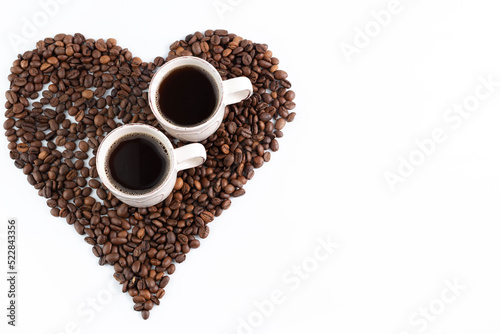 On a white background, a heart made of coffee beans and two cups of espresso. Background with place for writing text. View from above.