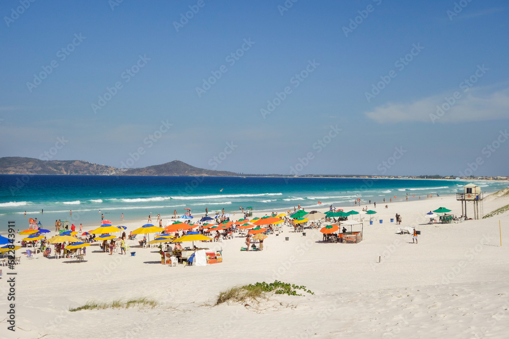 colorful umbrellas and tourists crowd the sand line at Praia do Forte in Cabo Frio, Rio de Janeiro, Brazil