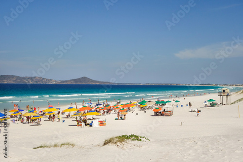 colorful umbrellas and tourists crowd the sand line at Praia do Forte in Cabo Frio, Rio de Janeiro, Brazil © Caio
