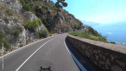 first-person view, moto rides along a serpentine road along the Amalfi coast Italy on the Mediterranean Sea. Drone follows moto. Trave destination in Italy. August 2022