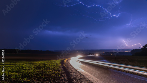 Gewitterblitze über einer Strasse, wo Autoscheinwerfer Leuchtspuren hinterlassen, Langzeitbelichtung