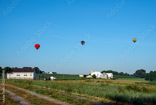 Hot air balloons rise in the sky behind an Amish school in the early morning hours of on a summer day. 