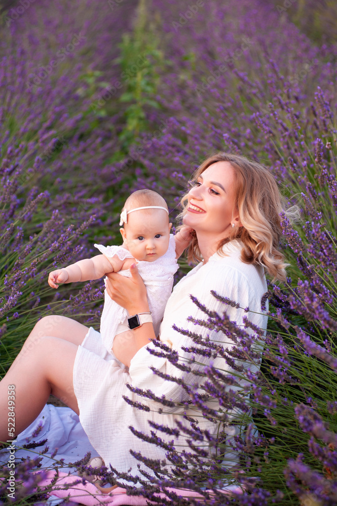 Happy mother with pretty daughter on lavender background. Beautiful woman and cute baby sitting in meadow field. Family holiday in summer day. Happy mother with pretty daughter on lavender background. Beautiful woman and cute baby sitting in meadow field. Family holiday in summer day.