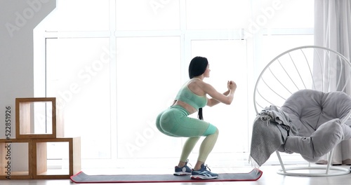 Young woman training with elastic resistance rubber band, beautiful female doing exercises alone at home, workout indoors