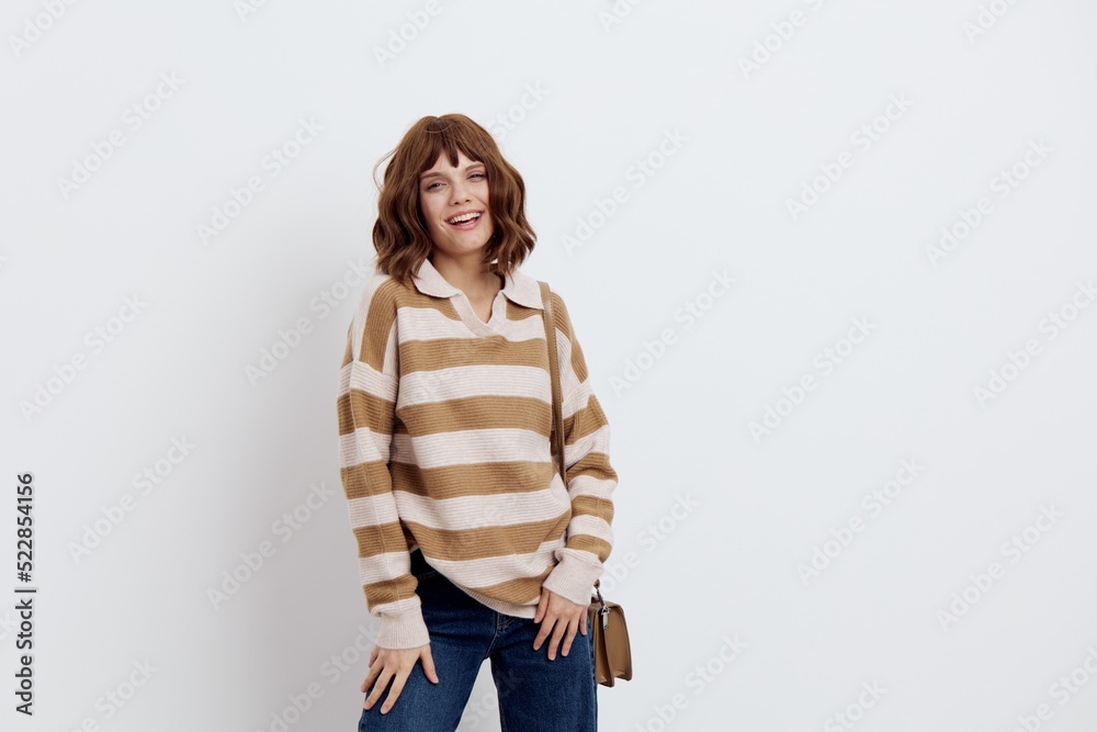 an emotional woman stands on a white background in a striped sweater and a bag on her shoulder, lowered two hands down, putting them on her feet an emotional woman stands on a white background in a striped sweater and a bag on her shoulder, lowered two hands down, putting them on her feet