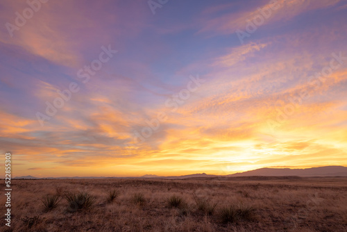 Vivid yellow sunrise over dry grassy plains with distant mountains at sunrise